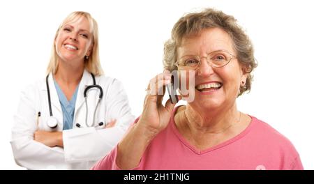 Donna anziana felice usando il telefono delle cellule con il medico femminile o infermiera dietro isolato su uno sfondo bianco. Foto Stock