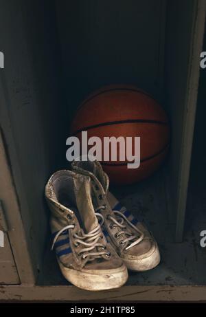 Primo piano di scarpe da ginnastica sportive vecchie e una palla da basket nell'armadietto, vista ad angolo alto Foto Stock
