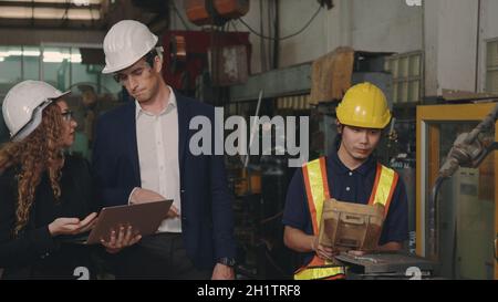 Tre heavy industry business engineering in hardhats discutere di informazioni su computer portatile mentre si è in piedi in interni di saldatura industriale f Foto Stock