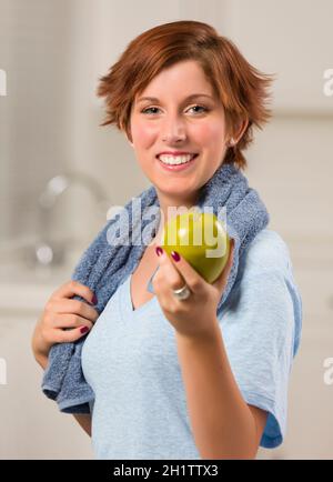 Piuttosto dai capelli rossi donna con asciugamano Azienda Mela Verde nella sua cucina. Foto Stock