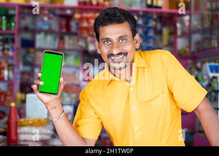 Sorridente Merchant al negozio di alimentari tenere mobile con schermo verde mock up guardando la macchina fotografica - concetto di tecnologia, pubblicità, prenotazione online Foto Stock