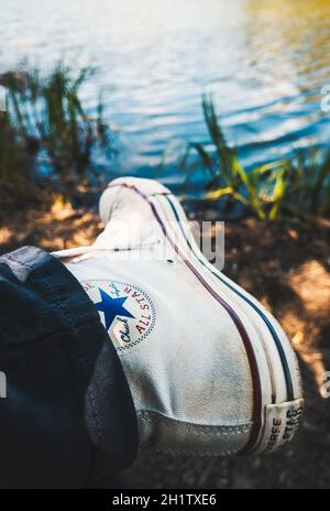 BIARRITZ, FRANCIA - CIRCA APRILE 2021: Indossato bianco Converse Chuck Taylor tutte le sneaker Star, riva del lago sullo sfondo. Foto Stock