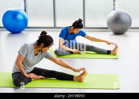 Due donne asiatiche sportive attraente persone che praticano yoga lezione insieme, allenarsi alla PALESTRA fitness, giovani e donne anziane esercizio Do yoga i Foto Stock