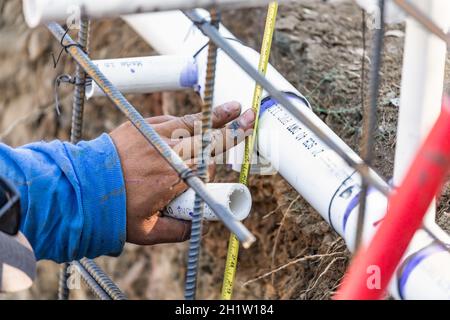 Plumber utilizzando nastro di misurazione durante l'installazione di tubo in PVC al sito in costruzione. Foto Stock