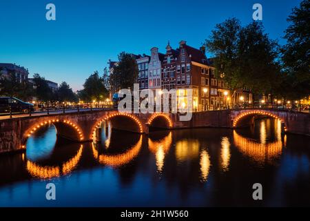 Vista notturna di Amterdam cityscape con canal, il ponte e le case medioevali nel crepuscolo della sera illuminata. Amsterdam, Paesi Bassi Foto Stock