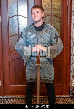 Un uomo vestito in un cavaliere del hauberk a casa nella sua stanza. Cavaliere del spada nelle mani di un uomo. Catena cavalleresco armor e spada. Il montaggio di un knightl Foto Stock