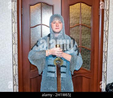 Un uomo vestito in un cavaliere del hauberk a casa nella sua stanza. Cavaliere del spada nelle mani di un uomo. Catena cavalleresco armor e spada. Il montaggio di un knightl Foto Stock