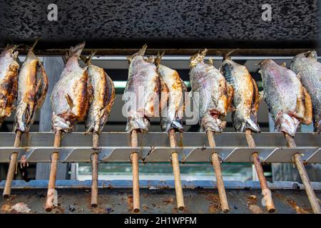 Disposizione di molti pesci su bastoni durante la cottura Foto Stock