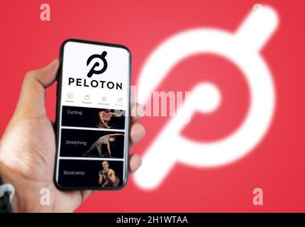 New York, USA, luglio 2021: Una mano che tiene un telefono con l'app Peloton sullo schermo. Sfondo rosso con logo Peloton sfocato. Peloton è un americano Foto Stock