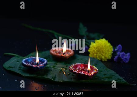 Eco-friendly artigianale colorato Clay Diya profondo o dia illuminato su foglia verde con fiori. Tema del Festival indiano per Diwali Pooja, Navratri, Duss Foto Stock