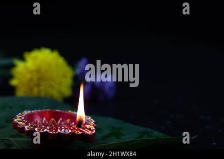 Primo piano di Eco friendly artigianale Red Clay Diya Deep o dia illuminato su foglia verde con fiori. Tema del Festival indiano per Diwali Pooja, Navratri Foto Stock