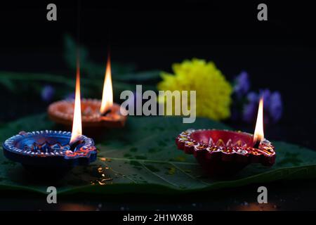 Eco-friendly artigianale colorato Clay Diya profondo o dia illuminato su foglia verde con fiori. Tema del Festival indiano per Diwali Pooja, Navratri, Duss Foto Stock