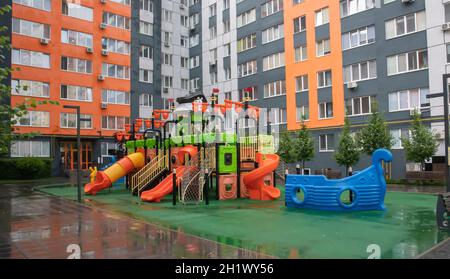 Un cortile di alti edifici con un nuovo e moderno parco giochi colorato e grande in una giornata estiva piovosa senza persone. Parco giochi all'aperto vuoto. A p Foto Stock