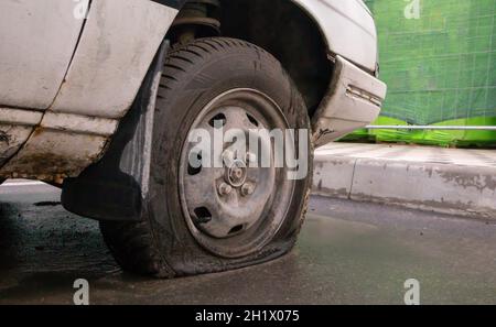 Abbandonata vecchia auto rotta con ruote piatte. Uno pneumatico con pneumatico sgonfio. Il concetto di incidente, guasto, riparazione, assicurazione. Uno pneumatico sgonfio su una ruota per auto Foto Stock