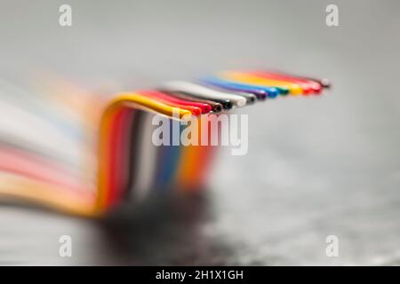 Primo piano di un cavo a nastro per computer corto, piegato e colorato su una superficie grigia ruvida con profondità di campo molto bassa. Foto Stock