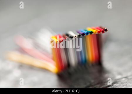 Primo piano estremo di un cavo a nastro per computer corto, piegato e colorato su una superficie grigia ruvida con profondità di campo ridotta. Foto Stock