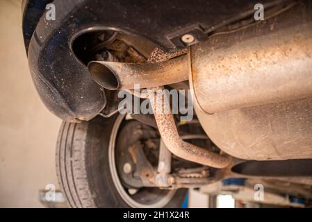 Dettaglio della vecchia marmitta arrugginita sotto un'auto in un'officina Foto Stock