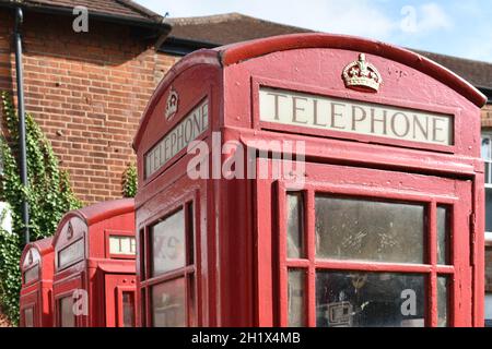 primo piano di 3 scatole telefoniche rosse d'epoca con corona reale d'oro in cima, in una strada fuori da un edificio in mattoni in estate Foto Stock