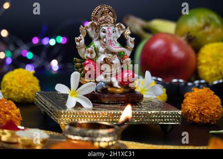 Statua colorata di Dio indù Ganesha Ganpati Bappa Morya seduta su Golden Asana con frutti, fiori, lampada e Blur Bokeh per il nuovo anno Diwali Puja Foto Stock