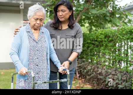 Aiuto e cura Asian anziani o anziani donna vecchia uso walker con forte salute mentre a piedi al parco in felice vacanza fresca. Foto Stock