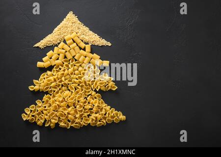 Albero di Natale creativo alternativo di pasta secca su sfondo nero. Biglietto di auguri natalizio con spazio per la copia. Vista dall'alto. Cibo Conc. Vacanza Foto Stock
