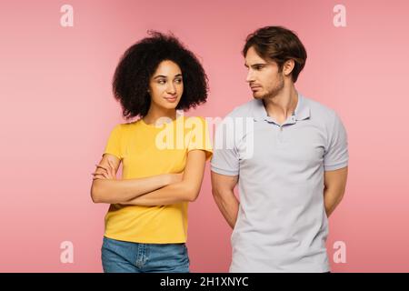 donna latina positiva e offeso uomo guardarsi l'un l'altro isolato su rosa Foto Stock