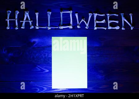 Scritta dalle ossa della parola Halloween e foglio bianco di carta su uno sfondo di legno blu. Design per celebrare il giorno di Halloween. Felice Foto Stock