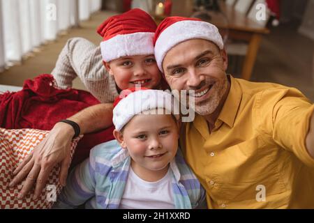 Il padre caucasico e due figli sorridevano mentre parlavano un selfie a casa durante il natale Foto Stock