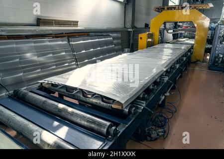 Nastro trasportatore o linea con tegole metalliche finite confezionate. Produzione industriale di coperture su attrezzature automatizzate. Foto Stock