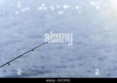 Canna da pesca su sfondo di acqua blu, fuoco selettivo con spazio di copia per il testo. Foto Stock