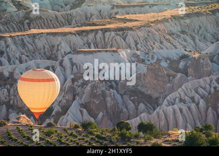 Paesaggio con mongolfiera bianca che sale sopra il panorama della valle Cappadocia nella luce del mattino con formazioni rocciose a camino nell'antenato Foto Stock