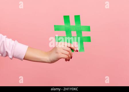 Primo piano di giallo hash segno, femmina mano che tiene carta hashtag, simbolo delle tendenze del social network e commenti popolari, famoso contenuto del blog, promozione. Studio interno girato isolato su sfondo rosa Foto Stock