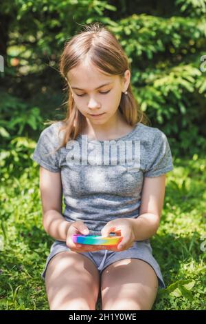 Ragazza di età che gioca silicone antistress popit fidget giocattolo all'aperto, concentrarsi su fidget Foto Stock