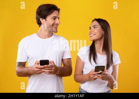 Coppia allegra usando i telefoni delle cellule che si levano in piedi allo studio Foto Stock
