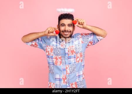 Bell'uomo in camicia blu con due piccoli sentori rossi nelle mani e angelico nimbus sopra la testa, guardando la macchina fotografica con un sorriso toothy. Studio interno girato isolato su sfondo rosa. Foto Stock