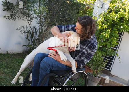 Uomo disabile caucasico seduto su sedia a rotelle giocando con il suo cane in giardino Foto Stock