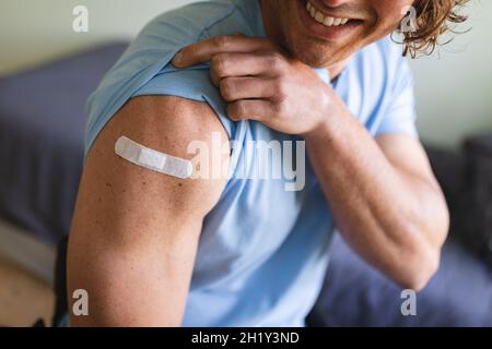 Metà della sezione dell'uomo disabile caucasico che mostra la spalla vaccinata a casa Foto Stock