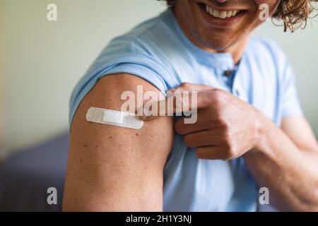 Metà della sezione dell'uomo disabile caucasico che mostra la spalla vaccinata a casa Foto Stock