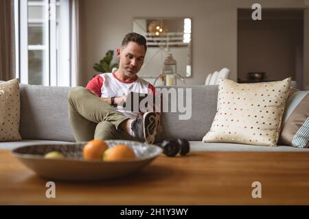 Uomo caucasico che usa un tablet digitale seduto sul divano di casa Foto Stock