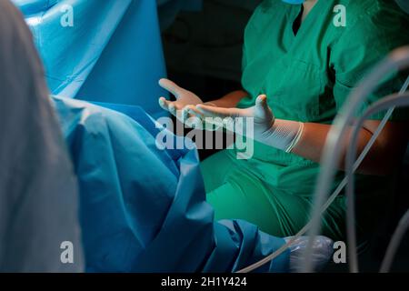 Mani del chirurgo in guanti sterili in lattice. Un chirurgo in uniforme verde tira in avanti le dita sparse in guanti chirurgici sterili. Le mani del chirurgo durante l'intervento chirurgico. Foto Stock