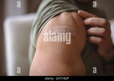 Metà della sezione dell'uomo caucasico che mostra la spalla vaccinata a casa Foto Stock