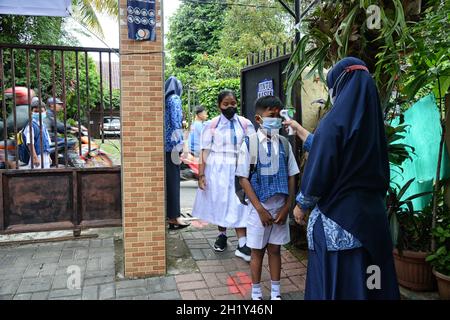 Un insegnante controlla la temperatura corporea di uno studente mentre altri sono in coda al loro arrivo alla scuola elementare Harjasari 01 a Bogor, West Java, Indonesia, il 18 ottobre 2021, come il governo ha permesso agli studenti di tornare alle loro scuole con nuove regole e di distanza sociale. (Foto di Adriana Adie/INA Photo Agency/Sipa USA) Foto Stock