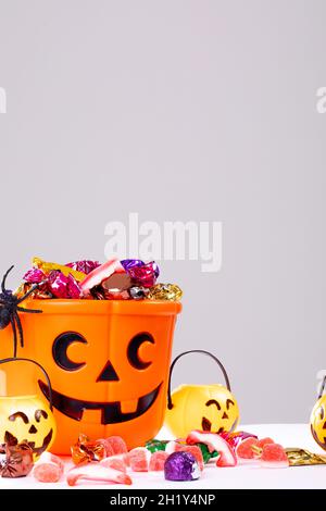 Composizione del secchio di Halloween con dolci trick o treat, ragno e zucche su sfondo bianco Foto Stock