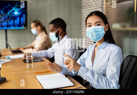 Asian Businesswoman indossare maschera medica applicazione spray disinfettante durante la riunione aziendale Foto Stock