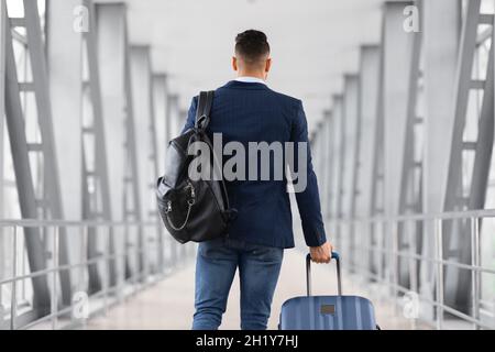 Vista posteriore del viaggiatore irriconoscibile di sesso maschile con zaino e valigia in aeroporto Foto Stock