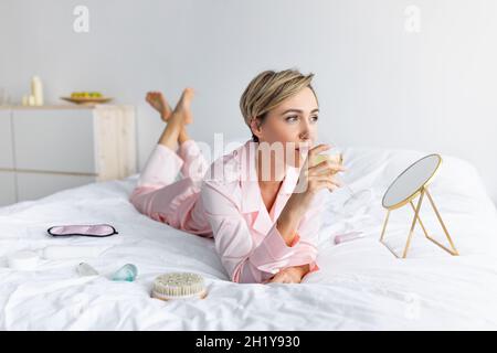 Ritratto di donna sdraiata a letto bevendo alcol Foto Stock