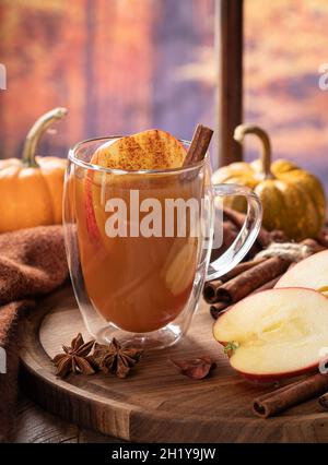 Tazza di sidro di mele e mele affettate su un piatto di legno con zucche da una finestra e sfondo autunno Foto Stock