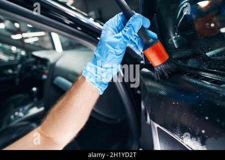 Detergente spargitore maschio sul finestrino dell'auto con spazzola