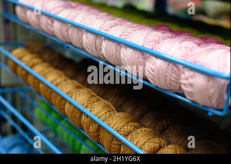 righe di palle di filati di cotone colorati per maglieria rosa pallido e senape sui ripiani del negozio Foto Stock