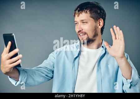 Un giovane sorride e invia messaggi di saluto su Internet utilizzando uno smartphone o un tablet. Mezzi e tecnologie moderne di comunicazione. Sfondo. Foto Stock